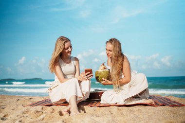 Arkadaşlar sahilde rahatlar, hindistan cevizi yudumlarlar ve yaz güneşinin altında akıllı telefonlarıyla birbirlerine bağlı kalırlar. Yüksek kalite fotoğraf