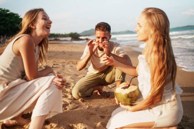 Arkadaşların neşeyle kahkahalarını ve ferahlatıcı hindistan cevizini yudumladıkları huzurlu bir sahil toplantısı. Yüksek kalite fotoğraf