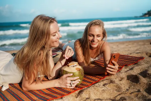 Arkadaşlar plajda soğuk içeceklerle rahatlar, telefonlarını karıştırır ve güneşli günün tadını çıkarırlar. Yüksek kalite fotoğraf