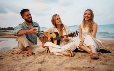 Arkadaşların keyifli bir şekilde gitar çalması, kahkahalarını paylaşması ve sahilde hatıralar yaratması.