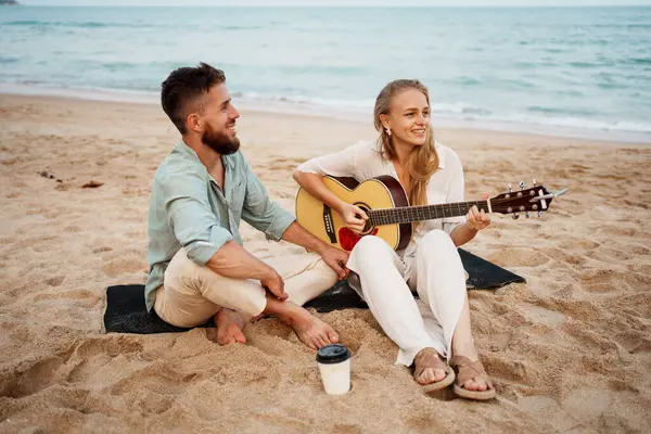 Neşeli bir çift güzel sahilde gitar çalıp deniz kenarında unutulmaz ve unutulmaz bir an yaratıyor.