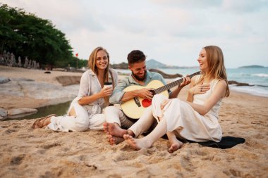 Bir grup arkadaş gün batımında plajda gitar çalarken keyifle keyifli bir anı paylaşıyorlar.