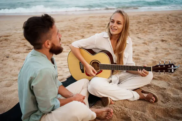 Bir çift, plajda bir gitarla neşeli bir an paylaşıyor. Altın saatinde kalıcı anılar yaratıyorlar.