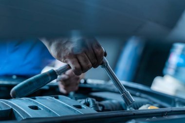 Bir araba motoru üzerinde soket anahtarı tutan bir el.