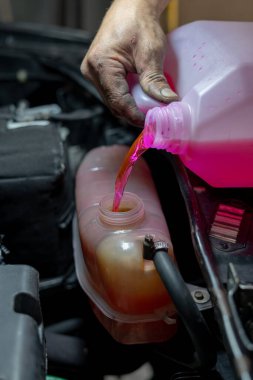 Tamirci el, araba radyatörüne pembe soğutucu döküyor.