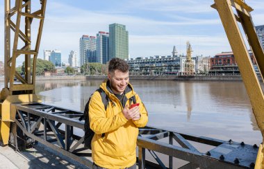 Genç Latin adam Puerto Madero 'da nehir kenarında akıllı telefon kullanıyor.