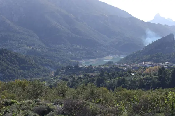 Fotoğraf, parçalı bulutlu bir gökyüzünün altında engebeli, kayalık tepeleri olan dağlık bir manzarayı gösteriyor. Dağlar ise dipdiri bir bitki (ler) ve hoş kokulu ağaçlarla kaplıdır. Ön planda..