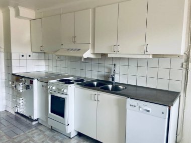 Beyaz dolapların olduğu mobilyasız bir mutfağın içi, döşeme kaplaması, fırın, bulaşık makinesi ve gündüz döşemeleri..