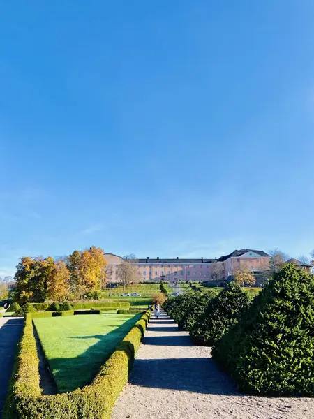 Uppsala Kalesi 'nin manzarası ve sonbaharda açık mavi bir gökyüzünde yakalanan barok tarzı botanik bahçeleri. Kesilmiş çalılar ve canlı sonbahar renkleri İsveç 'teki tarihi mekanın zarafetini vurguluyor.