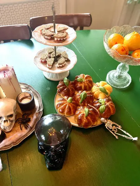 Balkabağı şekilli çörekler, kafatası süslemeleri, iskelet eller, içecekler ve yeşil bir masada şekerlemeler içeren stilize Cadılar Bayramı yemekleri. Cadılar Bayramı partileri, yemek blogları ya da mevsimlik kampanyalar için mükemmel bir ortam.