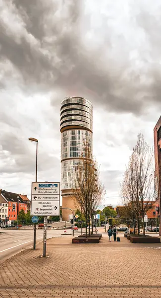 Baharın başında Bochum 'da bulutlu bir gökyüzüne karşı Exzenterhaus. Bir oğlan ve bir kız sırt çantaları ve küçük bir bavulla sokakta yürürler (arka manzara)).