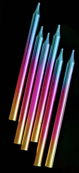 Siyah zemin üzerinde ince renkli mumlar (mavi, pembe, altın).