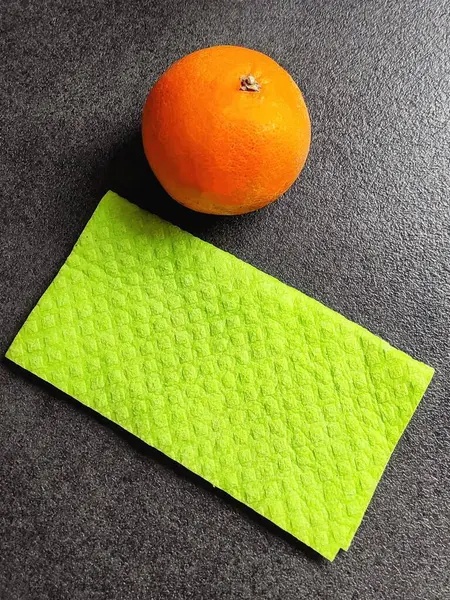 Parlak yeşil bir mikrofiber peçete ve siyah granit tezgahta bir portakal..