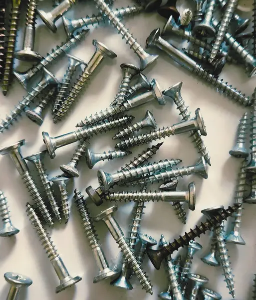 Farklı boyutlarda kendi kendine dokunan vidalar, hafif arka planda kaotik dağınıklıklar. Yapı malzemeleri, araçlar, onarım ve DIY kavramı.