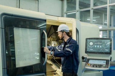 Akıllı fabrikadaki CNC makinesiyle otomatik robot eli kontrol eden dizüstü bilgisayar kullanan mühendis.