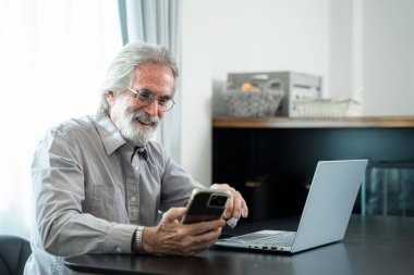 Üst düzey bir adam evinde dizüstü bilgisayarla rahat iş yerinde otururken cep telefonu kullanıyor emekli bir erkek sosyal medyadan arkadaşlarıyla sohbet ediyor..