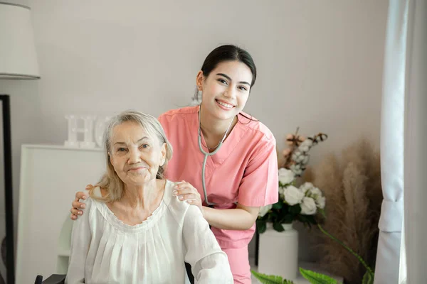 Gülümseyen kadın bakıcı yaşlı büyükanneme sağlık kontrolünde rehabilitasyon merkezinde yardım ediyor..