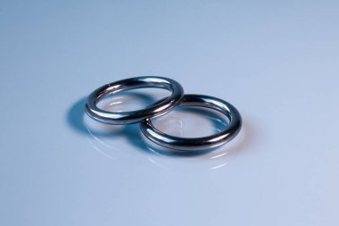 Çelik halkalar cam bir yüzey üzerinde uzanıyorlar. Görüntünün genel tonu açık mavi.