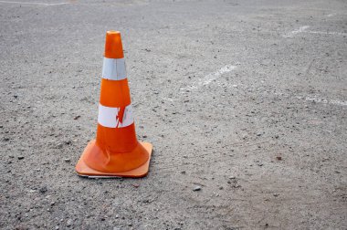 Turuncu trafik konileri asfalt yolda bir uyarı işareti olarak durmakta, bu da inşaat çalışmalarını ve güvenlik tedbirlerini işaret etmektedir