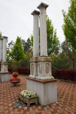 Dekoratif taş sütunları ön planda taze yeşillik ve renkli kaldırım taşlarıyla desteklenmiş.