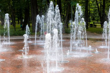 Çeşmenin sayısız su fıskiyesi kırmızı granitten yapılmış bir zemindeki gizli hortumlardan fışkırıyor..