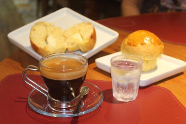 Zarif bir cam bardakta kaşıkla servis edilen bir fincan koyu espressonun yer aldığı hoş bir sahne. Kahveye iki yeni pişmiş çörek eşlik ediyor. Bir tanesi, çağdaş Whit 'in üzerinde sergilenen kremalı tereyağını gözler önüne sermek için kesilmiş.