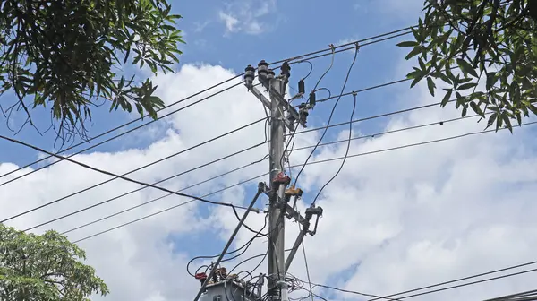 Elektrik kabloları olan bir elektrik direği bulutlu mavi bir gökyüzüne kurulmuş. Bu resim dış mekandaki elektrik hatlarının altyapısını yakalar