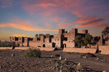 Kuru bir nehir yatağı (veya wadi) geleneksel kerpiç binaları kümesinin yanında uzanır. Muhtemelen bir köyün parçası olan binalar, güneşte kurumuş çamur tuğlalarından yapılmış ve karmaşık, dekoratif desenler sergiliyorlar. Birkaç kişi, muhtemelen Ziyaretçilerin sakinleri.