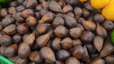 Canlı bir pazarda, kırmızımsı kahverengi pullu derisi ve eşsiz dokusuyla sergilenen taze bir yılan meyvesi yığını. Yemek, egzotik meyve ve tropikal pazar görselleri için mükemmel.!