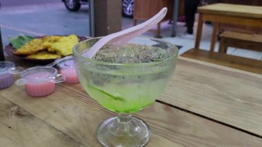 Yeşil şurup, limon ve fesleğen tohumlarıyla karıştırılmış cam bir kasede yenileyici bir Endonezya aloe vera tatlısı. Canlı renkler ve jöle gibi dokular onu yemek görselleri için mükemmel bir tropikal ikramdır.