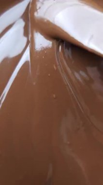 Zigzag desenli tereyağı kaşığıyla sürülmüş saf sıvı çikolatanın yakın çekimi. Hassas hareket, tatlı ve çikolatalı görseller için mükemmel. Gıda içeriği için dikey stok video.