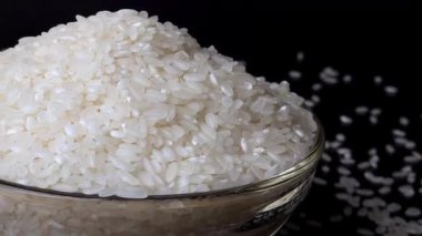 Cam kase köşesinde siyah yansıtıcı arka planda dönen pirinç taneleri var. Masanın etrafına saçılmış taneler. Detayları ve derinliği ekle.