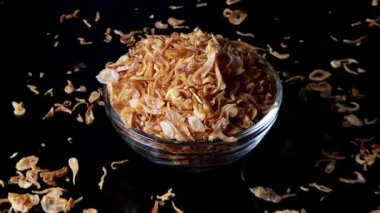 Siyah yansıtıcı bir yüzey üzerinde dönen kızarmış arpacık soğanlarıyla dolu orta boy cam kase. Dağıtılmış arpacık soğanları parlak yansıma detaylarıyla dokuyu güçlendirir