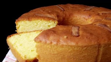 Beyaz havluyla ahşap tabakta dönen sünger kekinin yakın çekimi. Bir dilim kes ve pastaya yaslan. Siyah arkaplan yumuşak dokuyu vurgular