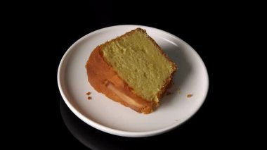 Beyaz tabakta siyah yansıtıcı yüzeyde dönen 45 derecelik sünger şeklinde bir kek. Yumuşak doku ve düz hareketle vurgulanmış altın kabuk