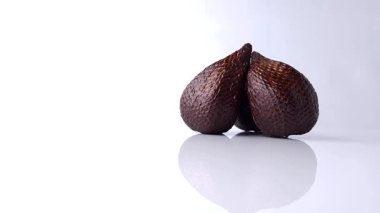 Çerçevenin sağ tarafında, parlak, beyaz yansıtıcı bir yüzeyde dönen üç adet meyveli meyve. Pürüzsüz doku ve parlak beyaz arkaplanda belirgin yansıma.