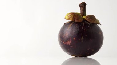 Beyaz yansıtıcı arka planda dönen, güçlü bir yansıması ve parlak beyaz arka planı olan, sağ tarafta oturan mangosteen meyvesini kapatın.
