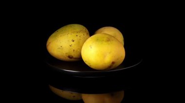 Siyah bir plaka üzerinde dönen üç taze mango. Altında güçlü bir yansıma var. Çerçevenin ortasında, siyah bir zemin üzerinde.