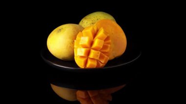 Siyah plaka üzerinde dönen üç mango, bir kesik kirpi stili, çerçeve merkezi, güçlü yansıma, koyu siyah arka plan