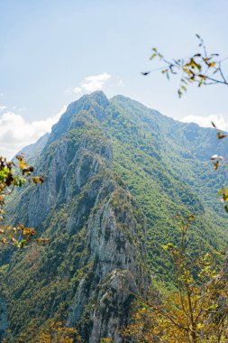 Arnavutluk 'un Tiran yakınlarındaki Bovilla Gölü' nde güneşli gökyüzünün altındaki yeşil kayalık dağ.
