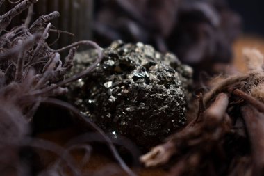 Koyu ahşap masada mum yakmak. Bir Pyrite kristali kümesi, ince dallar ve kuru yapraklar gibi doğal malzemelerle çevrili metalik bir ışıltıyla parlar. Piritin kübik oluşumları ışığı yakalar, yumuşak ile çelişir.