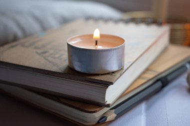 Mumlar ahşap bir yüzey üzerinde yanıyor, sıcak bir ortam yaratıyorlar. Yakınlarda, eskiz defterleri ve desenli bir yastığın üzerinde bir kalem istirahatı. Mum ışığı sahneyi hafifçe aydınlatıyor, samimi ve yaratıcı bir atmosfer izlenimi veriyor.. 