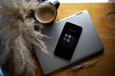 Kahve, telefon ve dizüstü bilgisayar üçlüsü üzerine yumuşak gölgeler. Doğal tonlarda sakin, üretken bir çalışma alanı..
