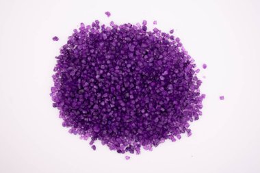 Temiz beyaz bir yüzey üzerinde canlı bir mor banyo tuzu yığını. Rahatlama, aromaterapi ve lüks bir spa deneyimini çağrıştırıyor.