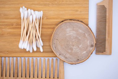 Çevre dostu bambu pamuk çubukları, doğal ahşap bir tarak ve bambu yüzeyinde yuvarlak bir tahta parçası. Sürdürülebilir ve dikkatli bir kişisel bakım rutinini benimse