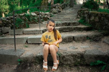 Eski harabeler ve yeşillik yakınlarındaki yıpranmış taş basamaklarda otururken akıllı telefona bakan genç bir kız tarihi ortamlarda, çocuklukta ve bireysel online aktivitelerde teknoloji temaları için idealdir.