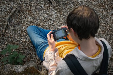 Bu görüntü, harabelerin yanındaki eski bir duvara yaslanırken akıllı telefon kullanan bir genci gösteriyor. Tarihsel ortamlarda, gençlik kültüründe ve gelişigüzel keşiflerde teknoloji temaları için ideal