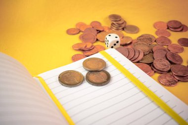Finansal kararların heyecanını yakalıyor, dağınık avro sikkeleri, bir günlük ve çarpıcı sarı bir zarı birleştiriyor. Mali planlama, risk alma ve strateji konuları için ideal