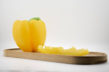 Sarı dolma biber, eşsiz bir şekilde ahşap bir tabanda ışık saçan dilimlerle sunulur, doğal canlılığı ve yenilikçi mutfağı sembolize eder. Mutfak sanatı, diyet ya da yemek ilhamı için ideal.