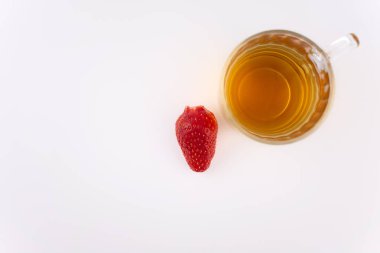 Canlı çileklerin yanında berrak bir bardak yeşil çay sükunet ve sağlıklı bir ferahlatıcı çağrıştırıyor. Detoks içeriği, rahat yaşam tarzı veya temiz yemek blogları için ideal